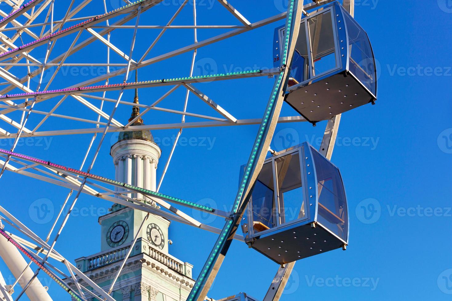 lege hutten van het reuzenrad van de stad tegen de achtergrond van de blauwe lucht en de torenspits van de oude toren. foto