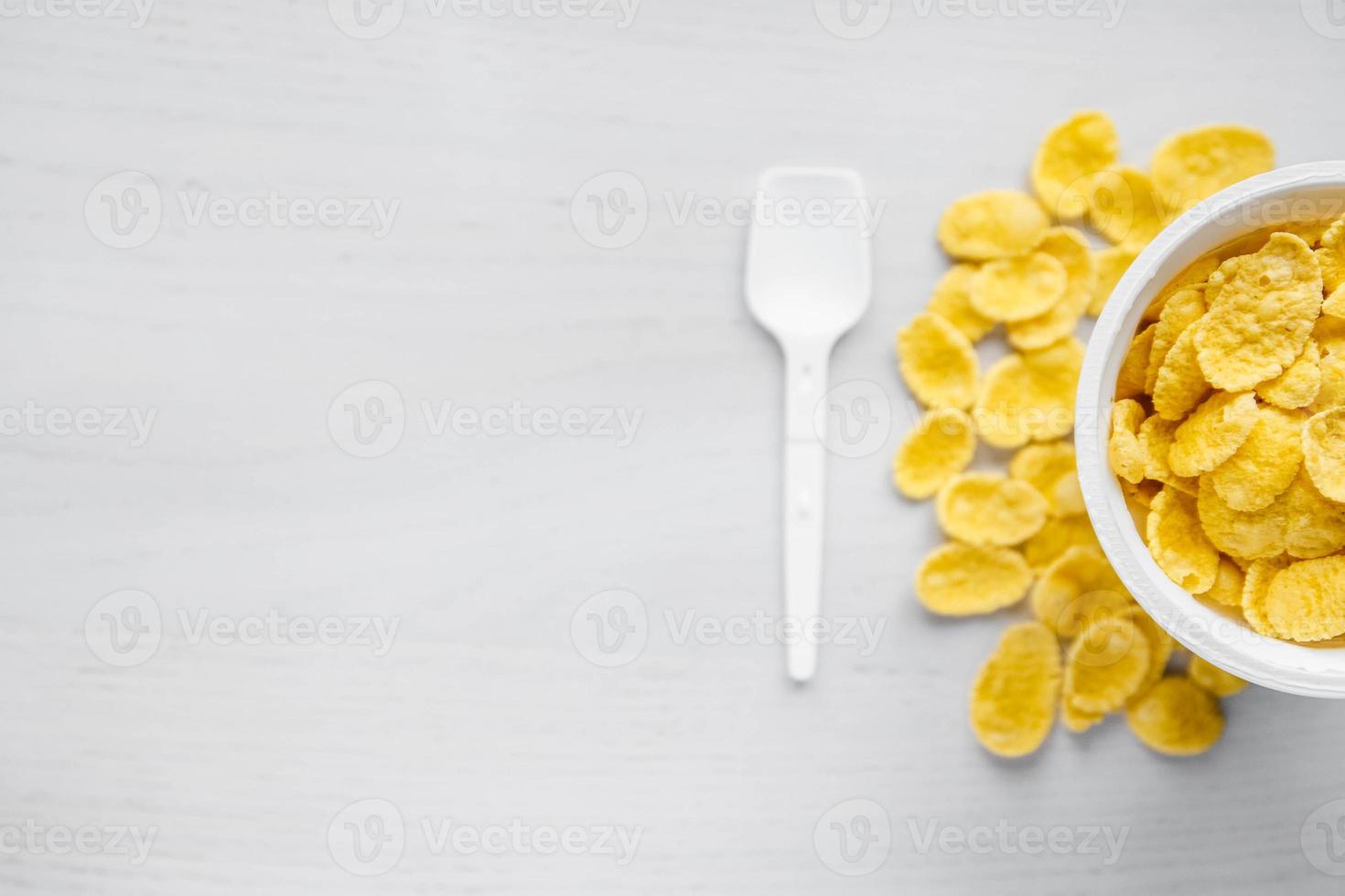 cornflakes in witte kom met lepel op witte houten achtergrond foto