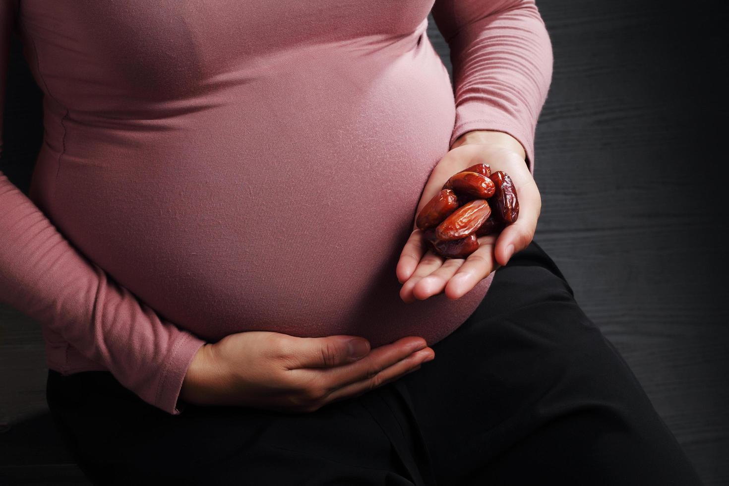 zwangere vrouw met dadelpalmfruit op zwarte achtergrond foto