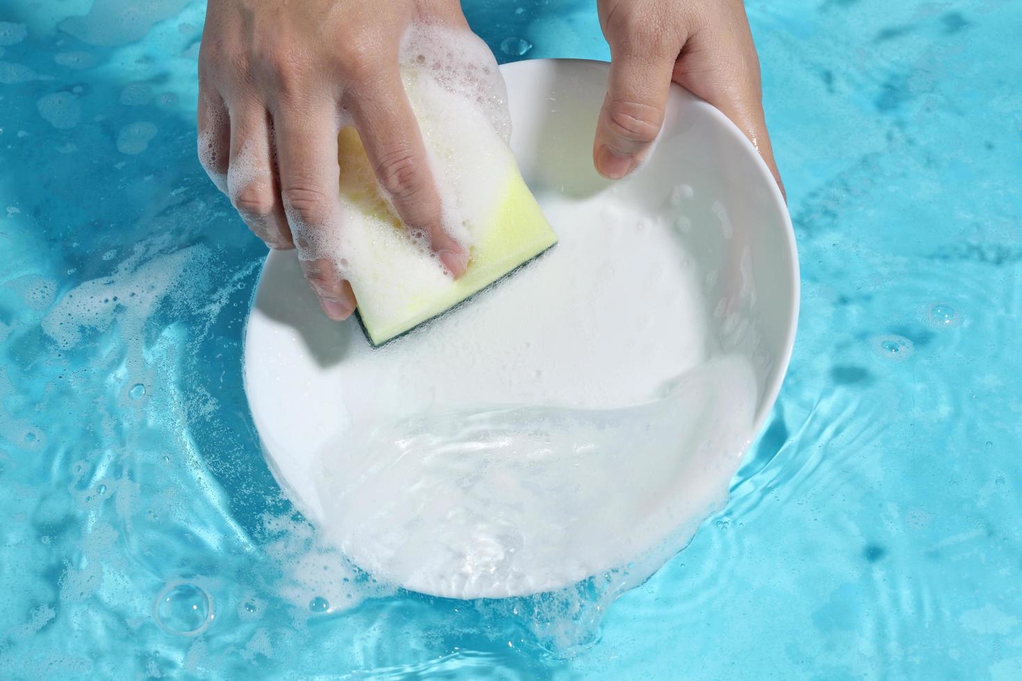 vrouw hand wassen keramische schotel in schoon water. foto