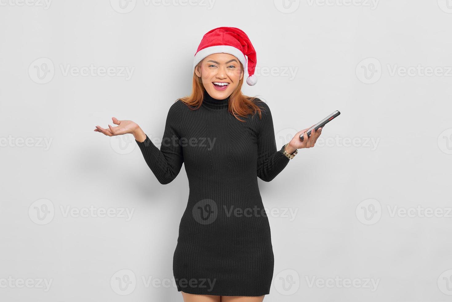 vrolijke, jonge, aziatische vrouw, in, kerstman hoed, vasthouden, gsm, en, vieren, geluk, geïsoleerde, op, witte achtergrond foto