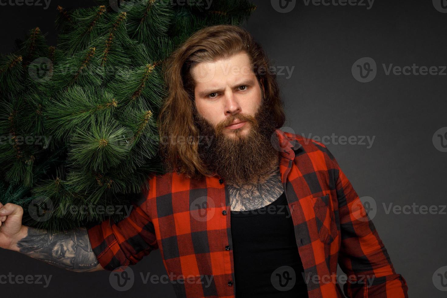 knappe man met lang haar die een synthetische kerstboom vasthoudt foto