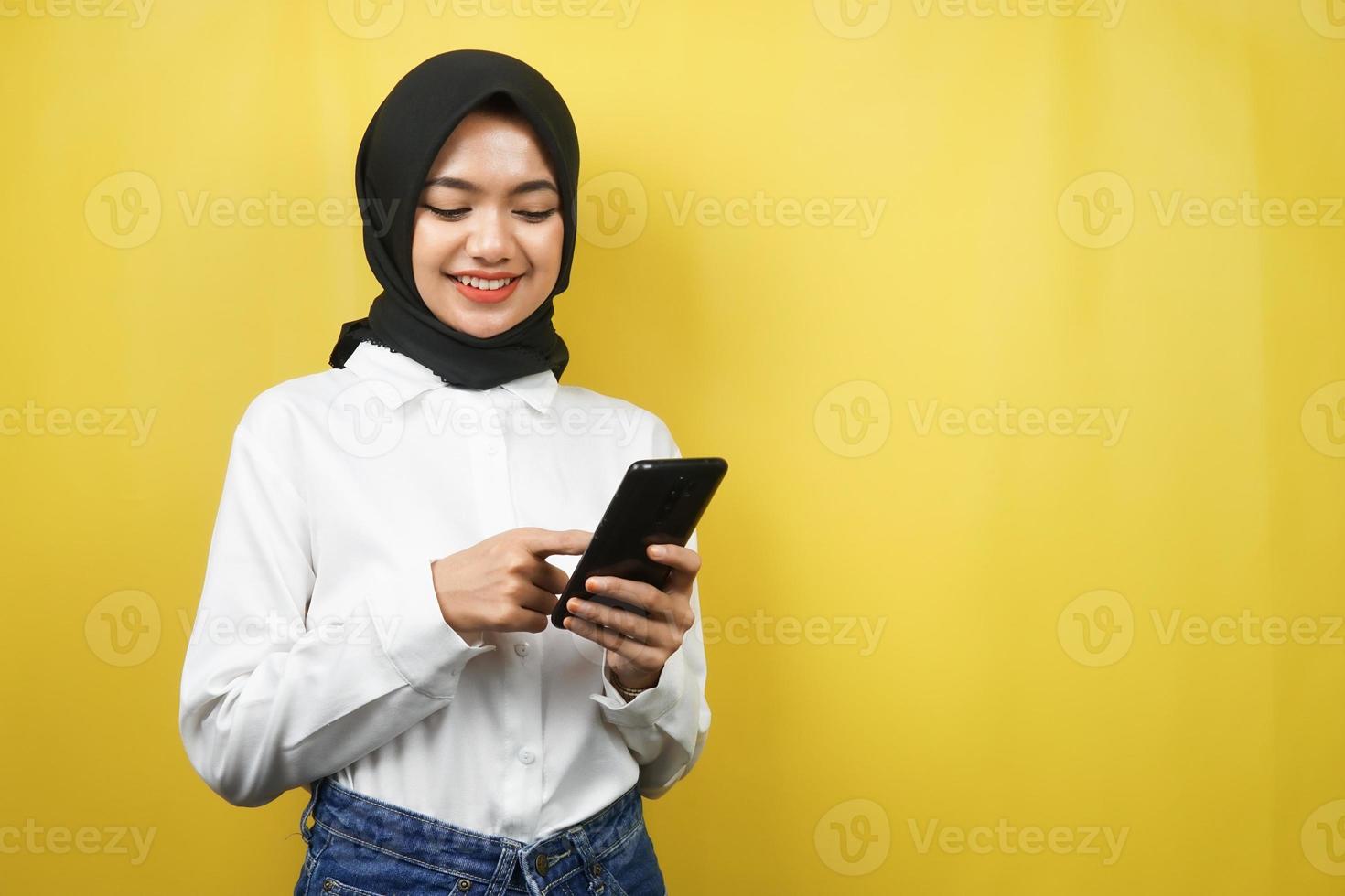 mooie jonge aziatische moslimvrouw die lacht en vol vertrouwen smartphone vasthoudt op een gele achtergrond, reclameconcept foto