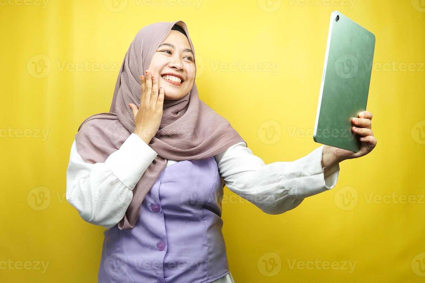 mooie jonge aziatische moslimvrouw die lacht, opgewonden en vrolijk met tablet, geïsoleerd op gele achtergrond foto