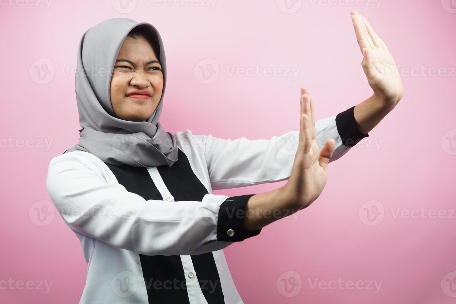 mooie aziatische jonge moslimvrouw met hand die iets afwijst, hand iets stopt, iets niet leuk vindt in lege ruimte, geïsoleerd op roze achtergrond foto