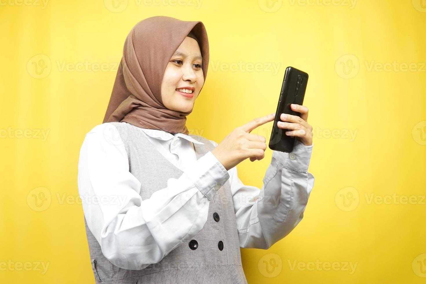 mooie jonge aziatische moslimvrouw die lacht en vol vertrouwen smartphone vasthoudt op een gele achtergrond, reclameconcept foto