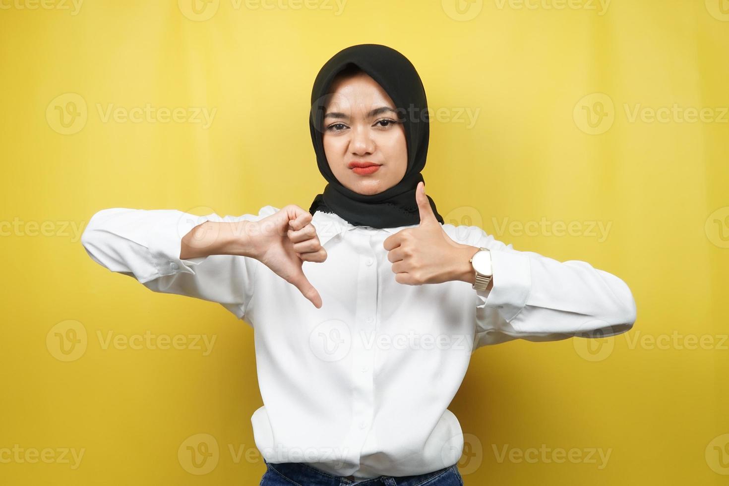 mooie Aziatische jonge moslimvrouw met handteken leuk of niet leuk, ja of nee, blij of verdrietig, twee dingen vergelijken, geïsoleerd op gele achtergrond foto