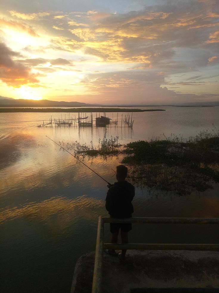 man visser vissen met een spinhengel in het meer in de middag. zonsondergang op limboto-meer, indonesië foto