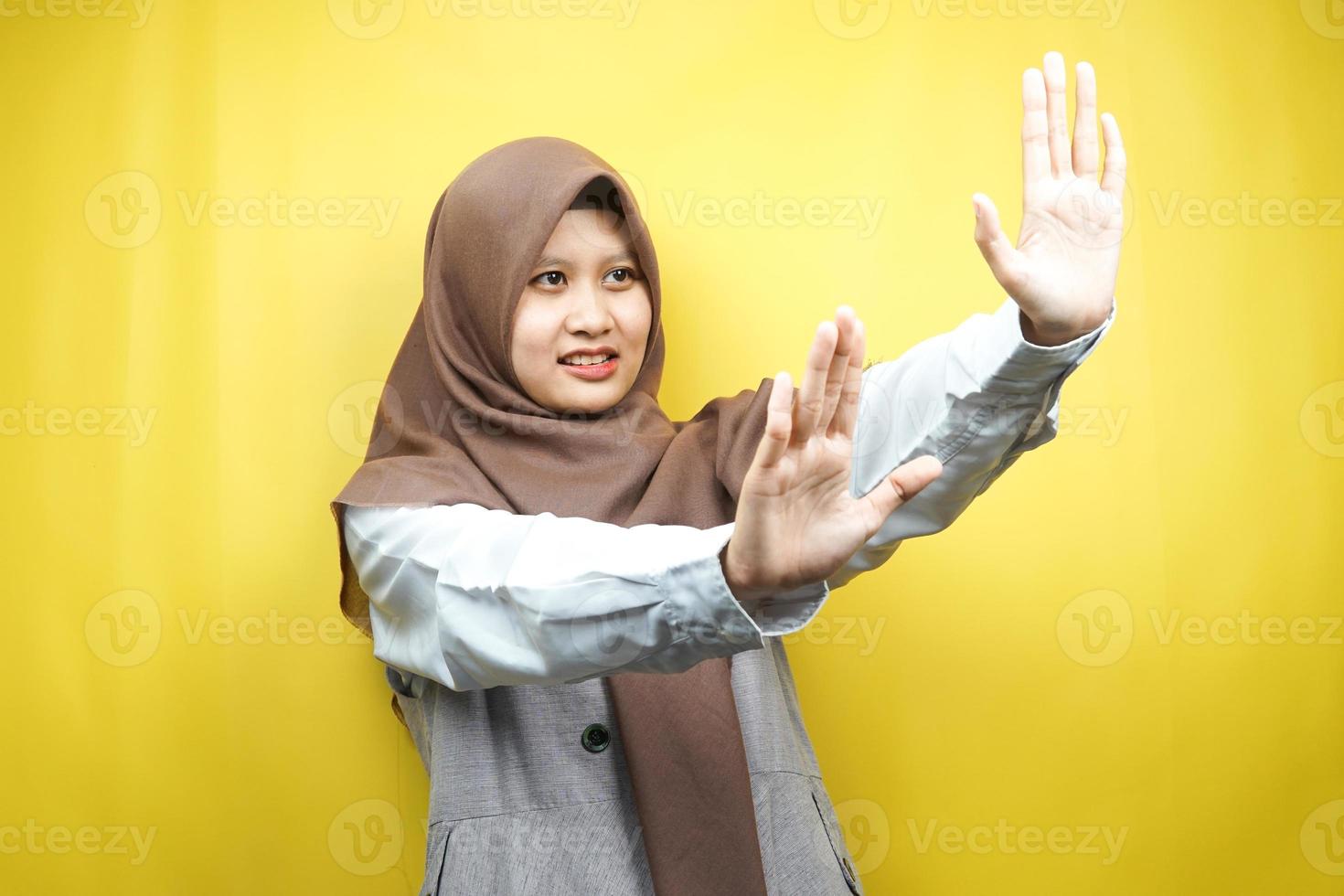 mooie aziatische jonge moslimvrouw met hand die iets afwijst, hand iets stopt, iets niet leuk vindt in lege ruimte, geïsoleerd op gele achtergrond foto