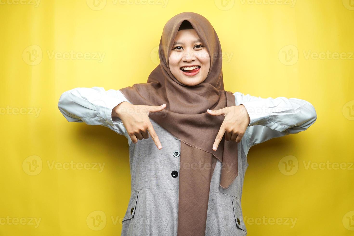 mooie aziatische jonge moslimvrouw met handen die naar beneden wijzen, handen klik op de onderstaande link, handen die iets presenteren, geïsoleerd op gele achtergrond foto