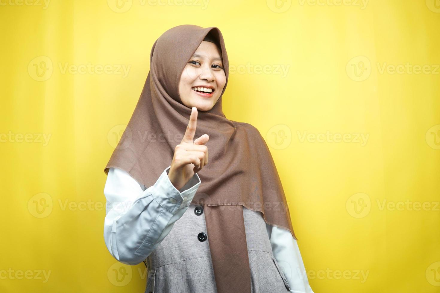 Mooie jonge Aziatische moslimvrouw glimlachend zelfverzekerd en vrolijk, met handen wijzend op camera, wijzend op publiek, wijzend naar klant, geïsoleerd op gele achtergrond foto
