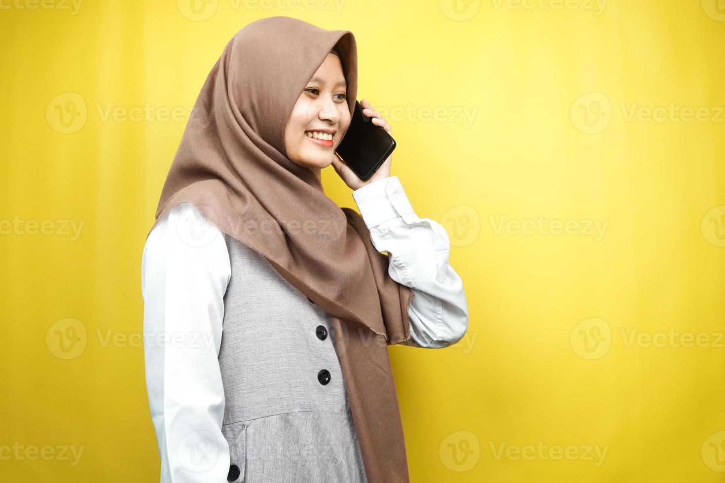 mooie jonge aziatische moslimvrouw die zelfverzekerd en vrolijk iemand belt, geconfronteerd met lege ruimte, geïsoleerd op gele achtergrond, reclameconcept foto