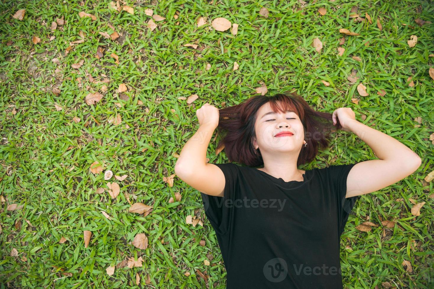 jonge aziatische vrouw die op het groene gras ligt en luistert naar muziek in het park met een koude emotie. jonge vrouw ontspannen op het gras met haar muziekafspeellijst. buitenactiviteit in het parkconcept. foto