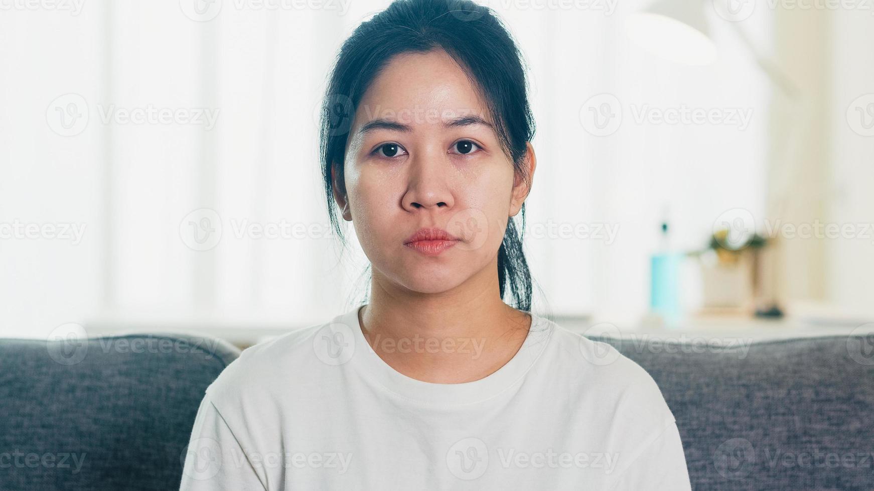 depressieve huilende aziatische zakenvrouw gestrest met hoofdpijn zittend op de bank in de woonkamer thuis wanneer sociale afstand thuis blijft en zelfquarantainetijd, coronavirusconcept. foto