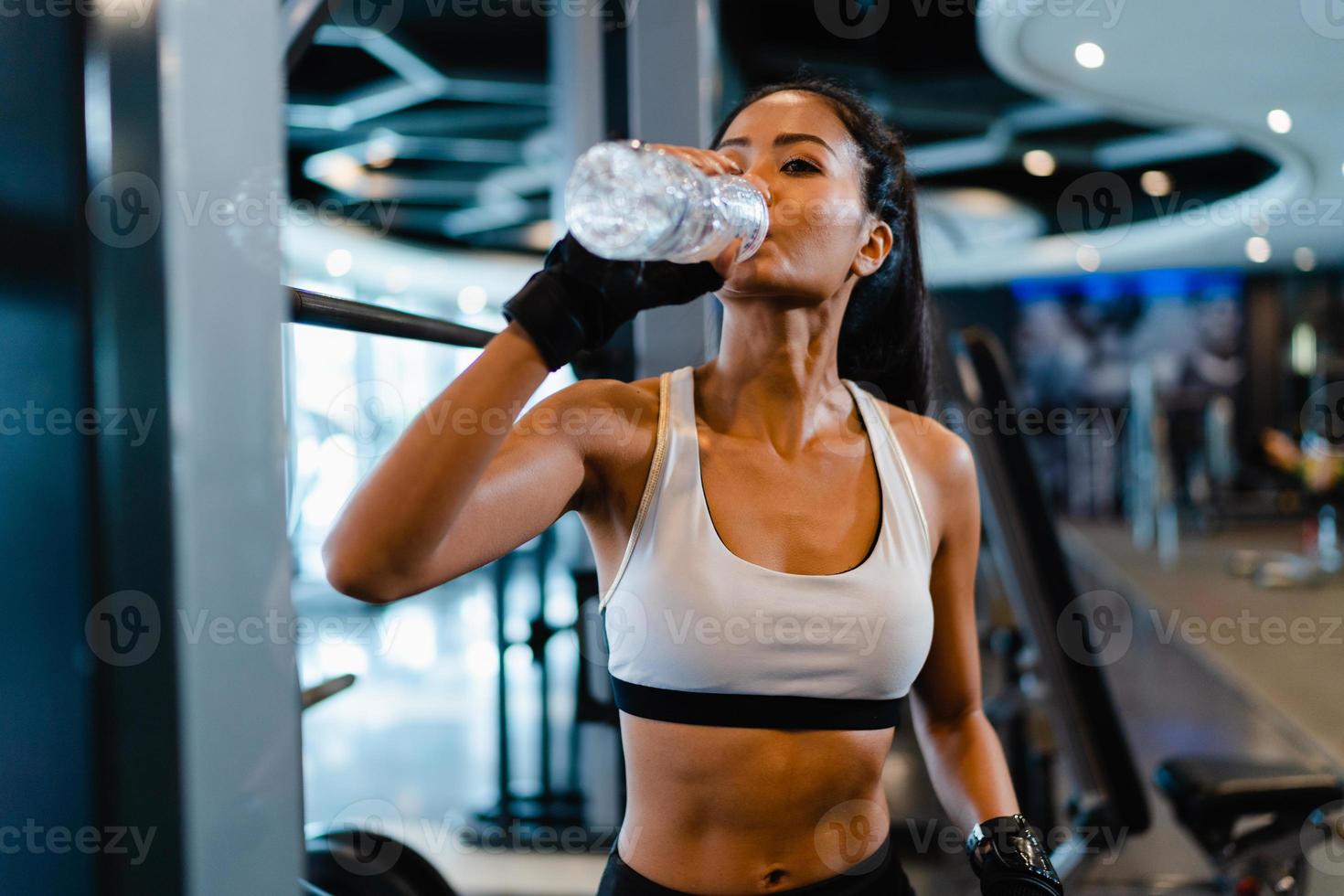 mooie jonge aziatische dame oefent drinkwater uit na vetverbrandende training in fitnessles. atleet met sixpack, sportvrouw recreatieve activiteit, functionele training, gezond levensstijlconcept. foto