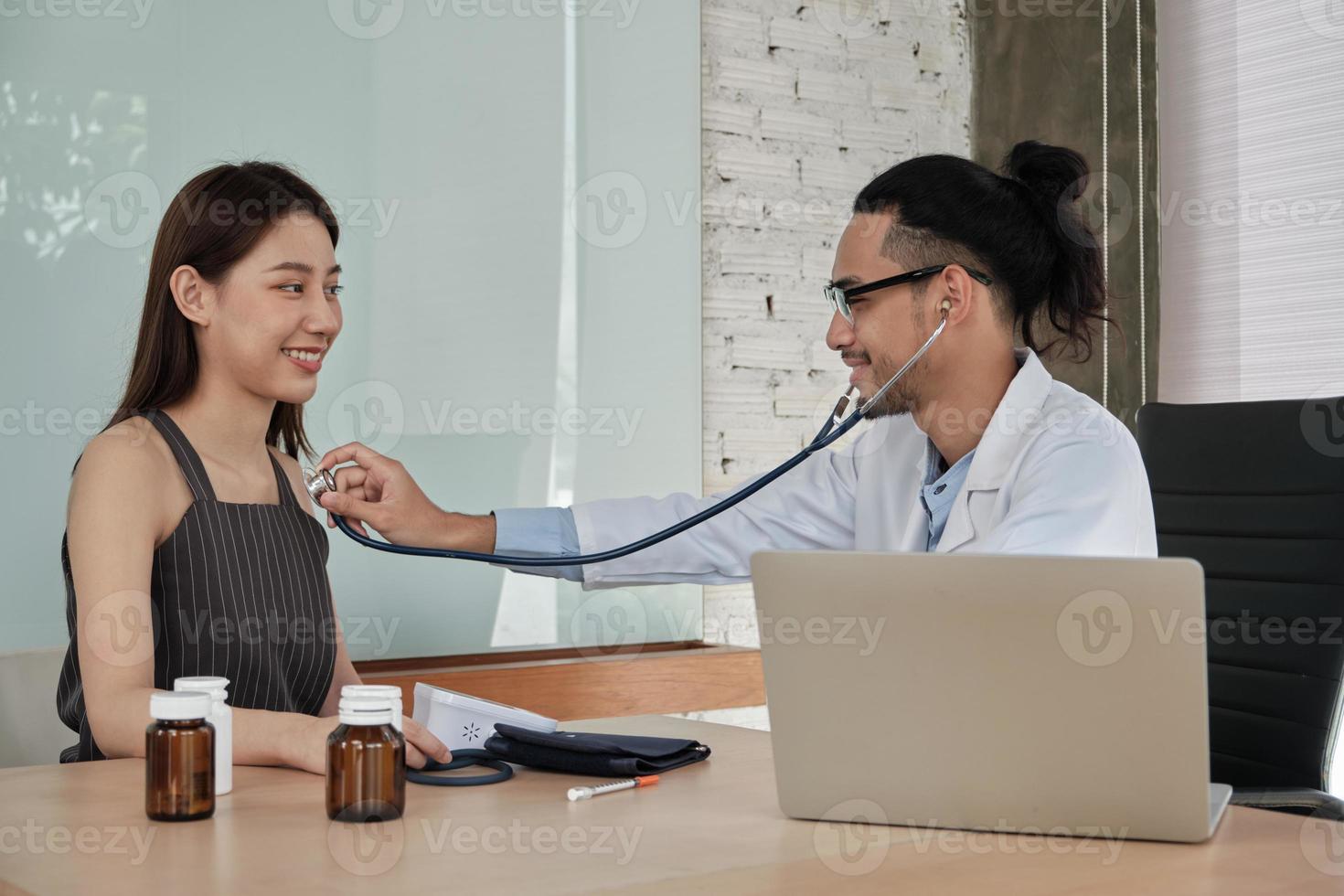 medische behandeling en controle, een jonge mannelijke arts onderzoekt een vrouwelijke patiënt van Aziatische etniciteit met een stethoscoop, adviseert een afspraakbezoek voor een gezondheidsconsult in een kliniek in een ziekenhuis. foto