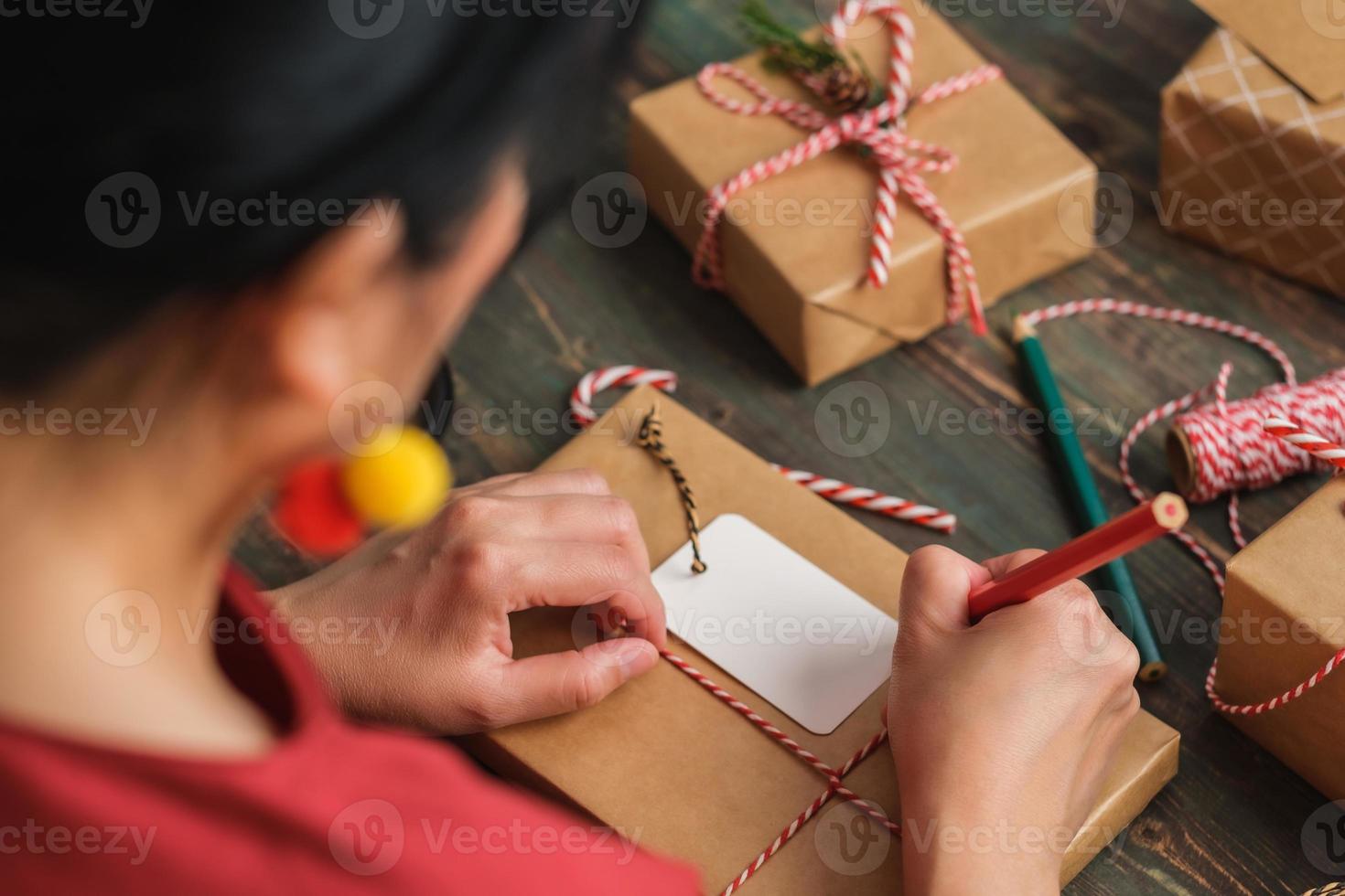 vrouw schrijft cadeau-tag en bevestig aan kerstcadeau op houten tafel foto