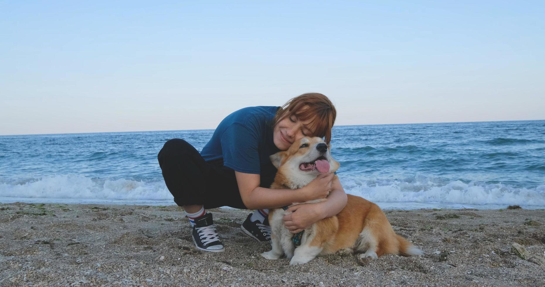 jonge vrouw speelt met corgi-hond op het zeestrand foto