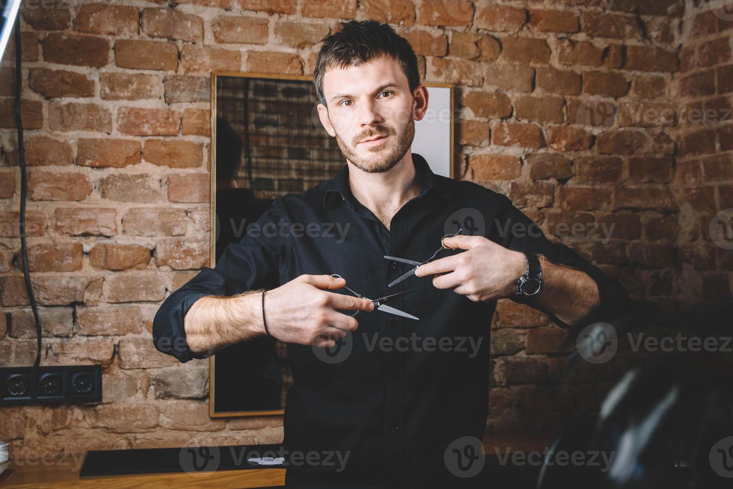 portret mannelijke kapper houdt een scherpe schaar tegen de achtergrond van een bakstenen muur foto