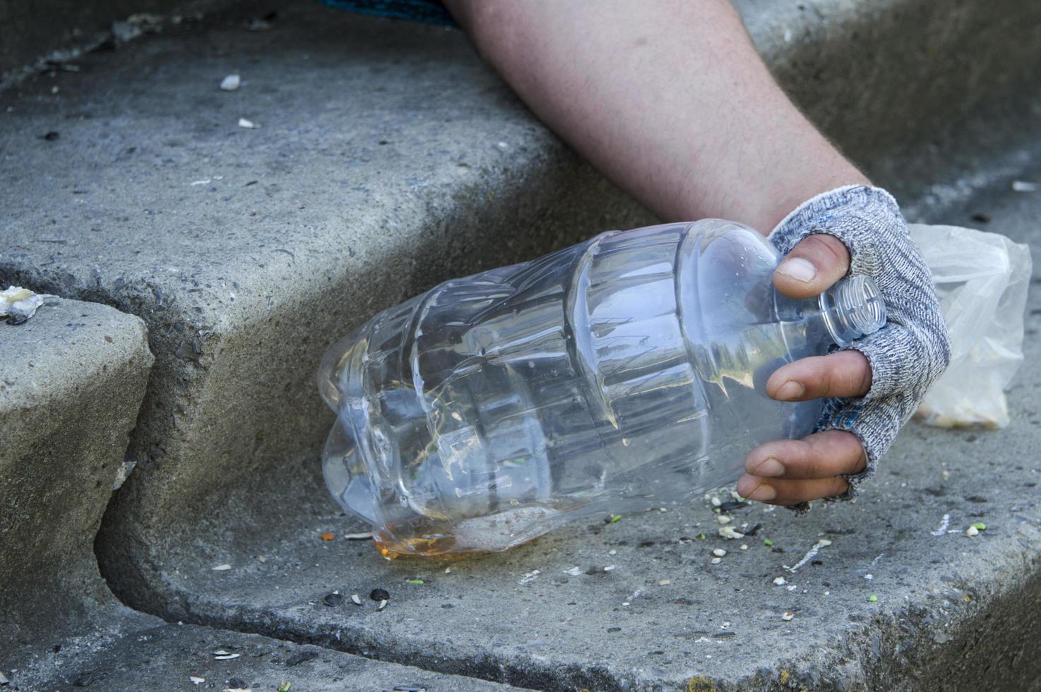 de gehandschoende hand van een dakloze op een lege bierfles. armoede, werkloosheid, alcoholisme. foto