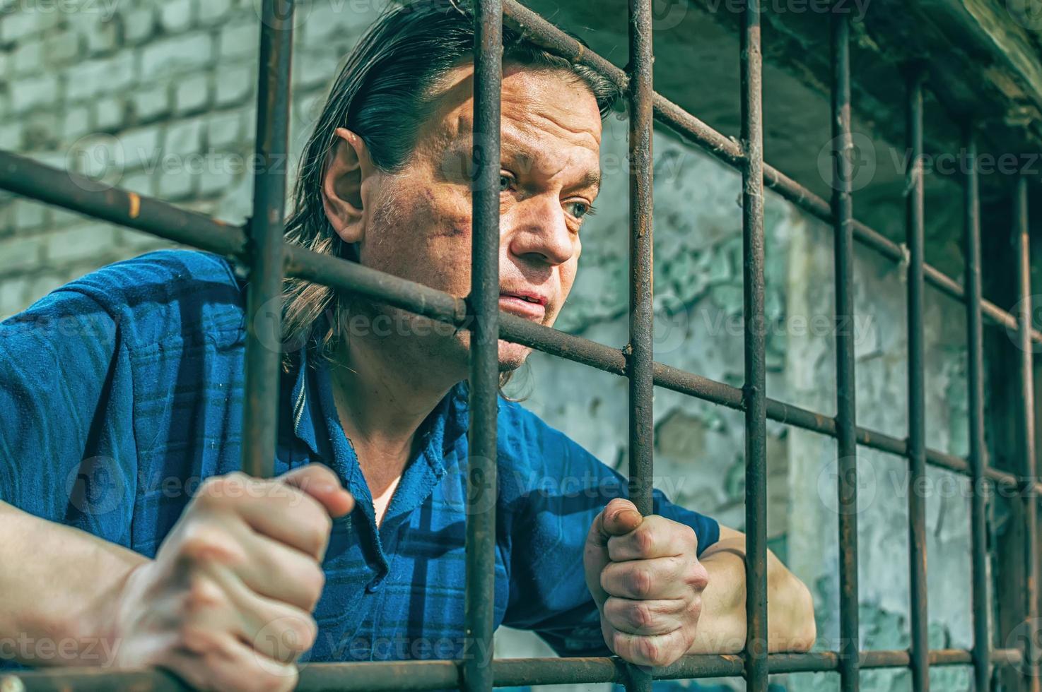 een depressieve man houdt zijn handen op de tralies van de gevangenis. gevangene voor de misdaad. slechte condities. schreeuwen, wanhoop, pijn, honger. foto