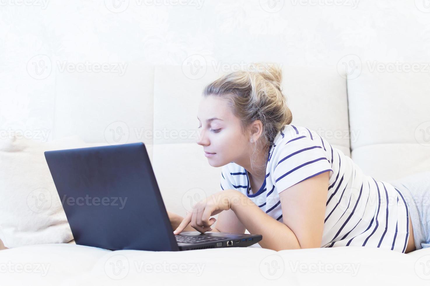 blond meisje zit thuis op de bank met een laptop en communiceert op internet. sociale netwerken. daten. foto