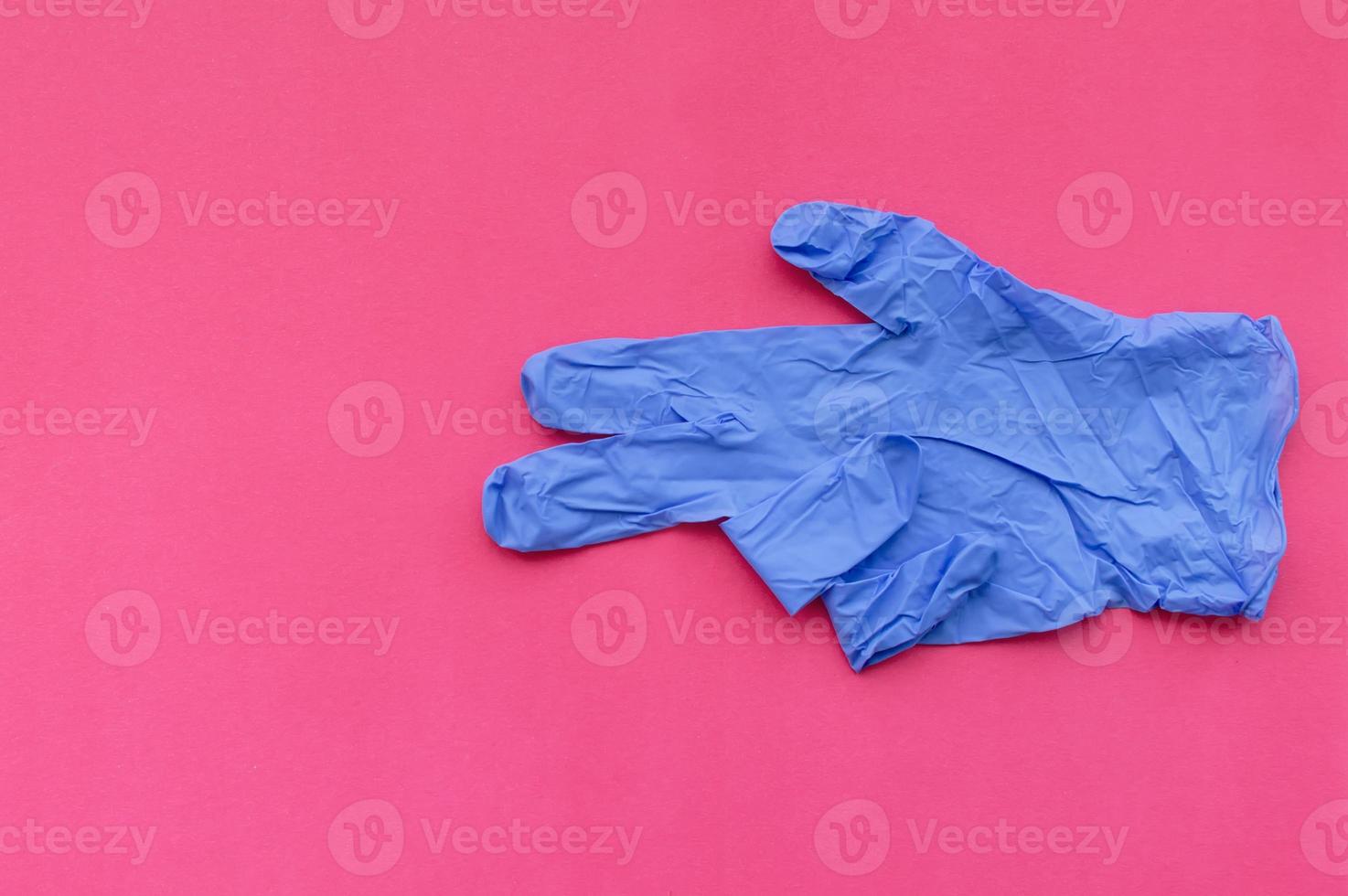 een blauwe medische handschoen op een roze achtergrond wijst met twee vingers naar een lege ruimte voor tekst. selectieve aandacht. foto