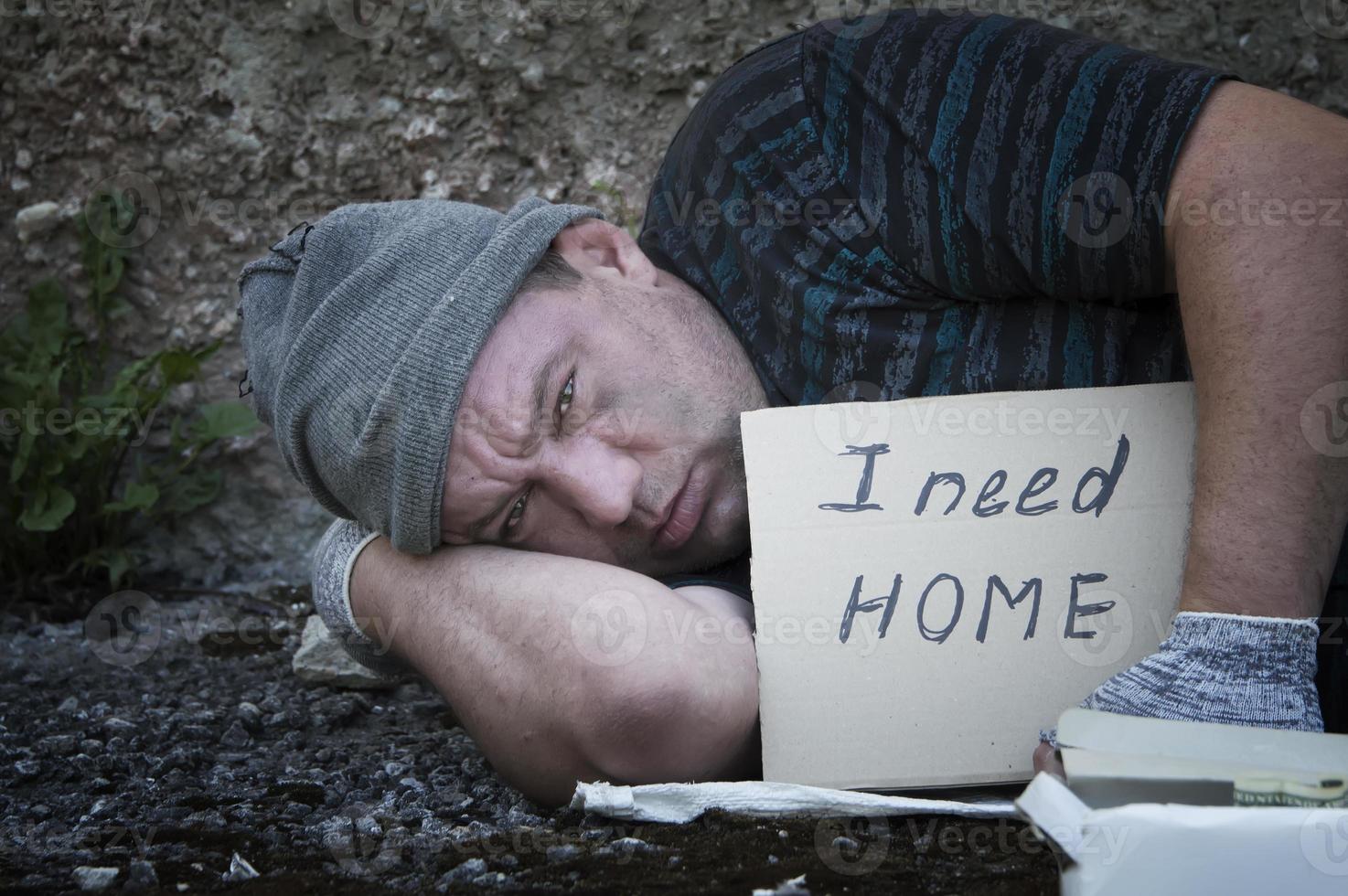 een dakloze man ligt op straat met een bord waarop staat dat ik een huis nodig heb. Armoede, ellende, werkloosheid. foto