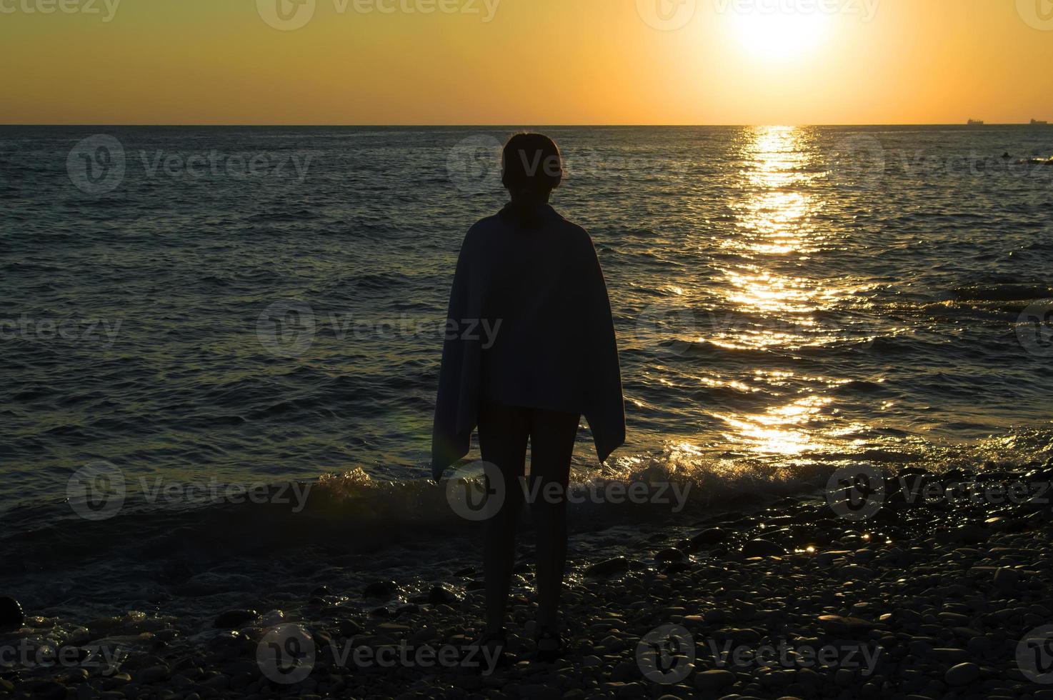 het silhouet van een kind tegen de achtergrond van een zonsondergang aan de kust. eenzaamheid. foto