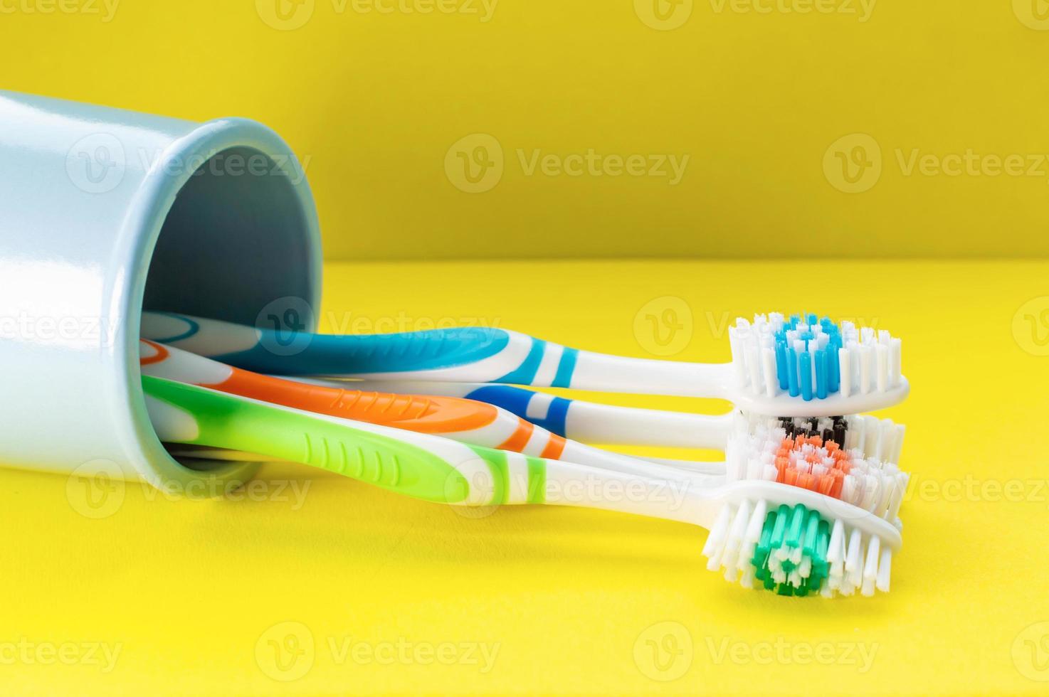 veelkleurige tandenborstels in een blauw glas op een gele achtergrond. detailopname. foto