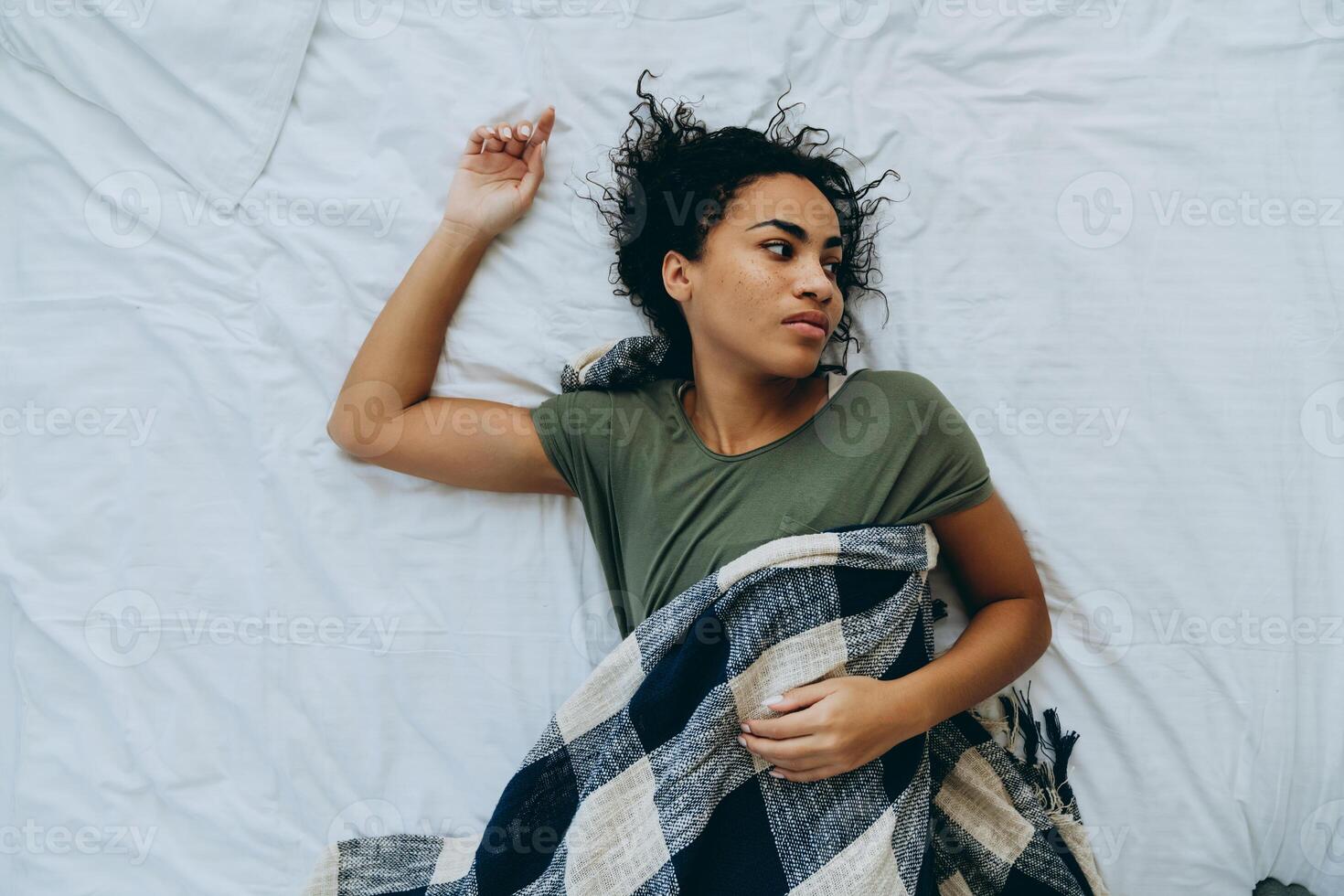 bovenaanzicht van vermoeide Afrikaanse vrouw wikkelde zichzelf in een deken en keek naar de zijkant foto