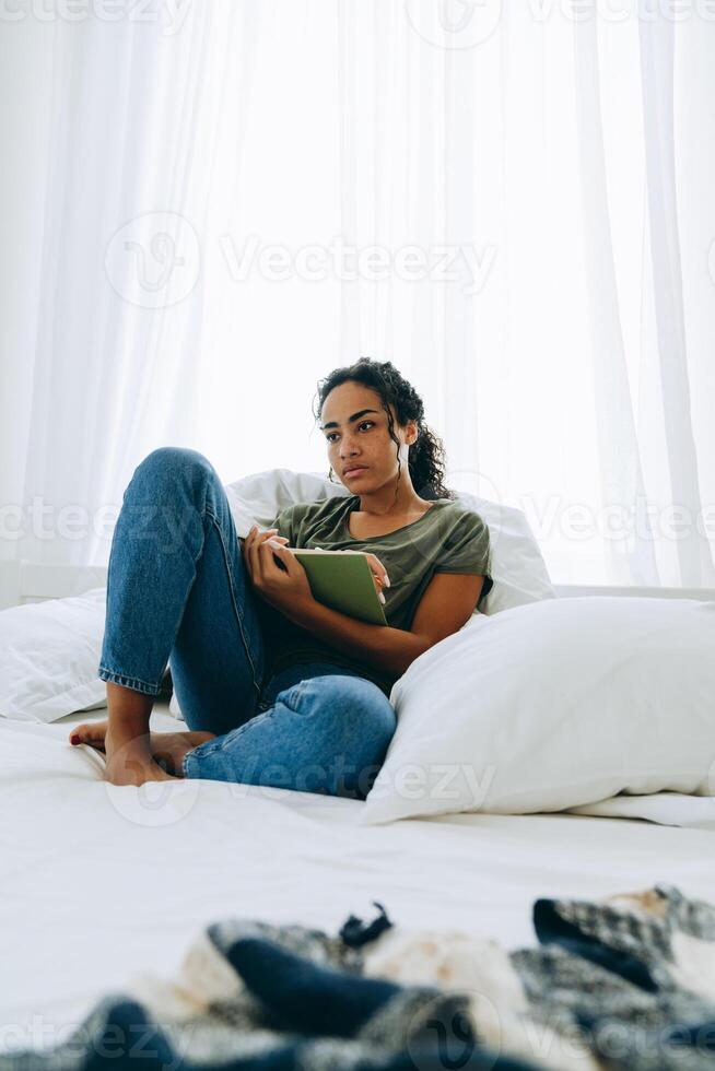 trieste Afrikaanse vrouw die iets in Kladblok op het bed schrijft foto