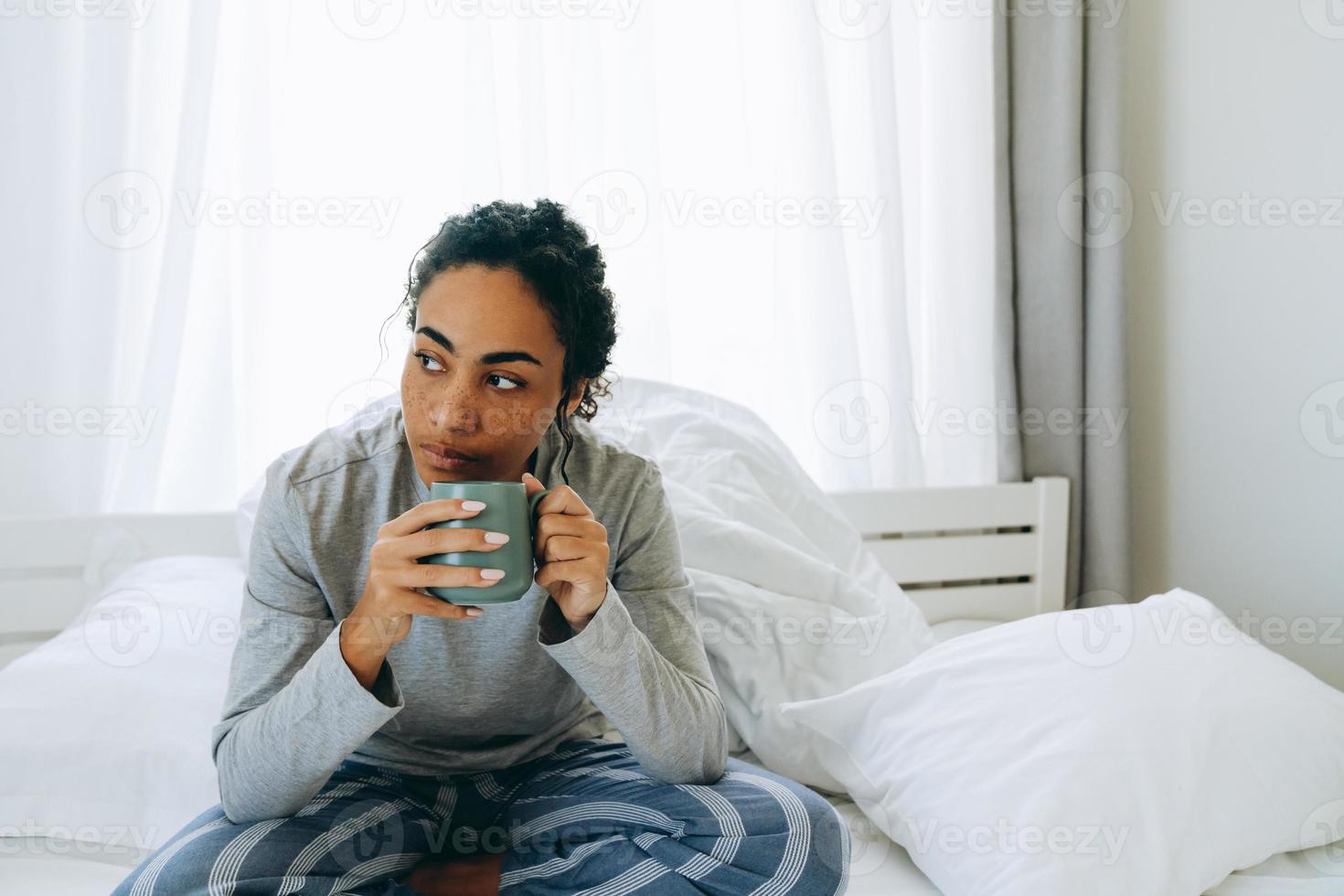 geconcentreerde Afrikaanse vrouw die koffie drinkt en naar de zijkant kijkt foto