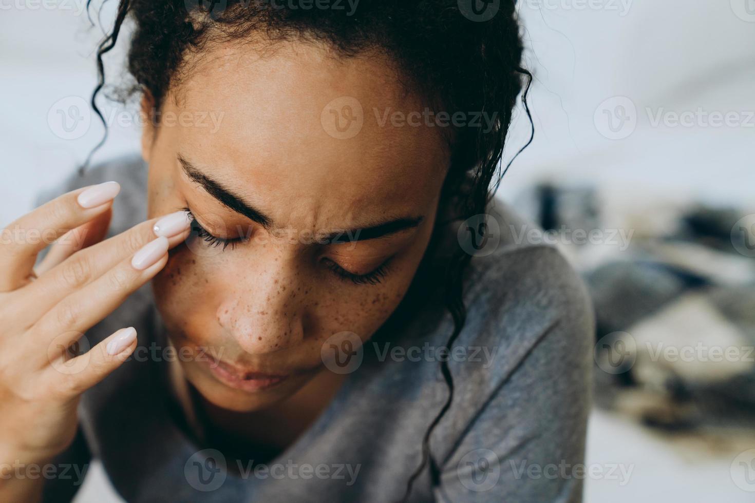 jonge zwarte vrouw huilt en veegt haar tranen af terwijl ze op bed zit foto
