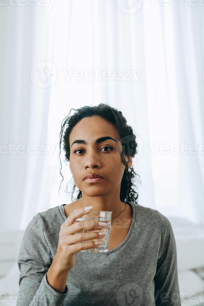jonge zwarte vrouw die water drinkt tijdens de tijd thuis foto