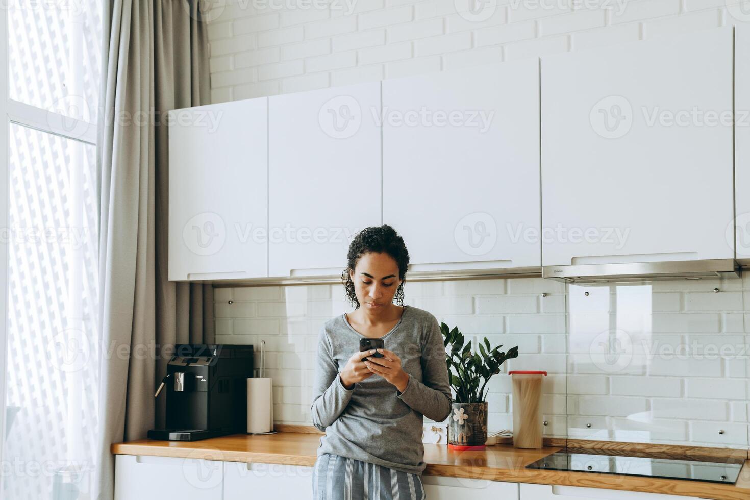 zwarte vrouw die mobiele telefoon gebruikt terwijl ze in de keuken staat foto