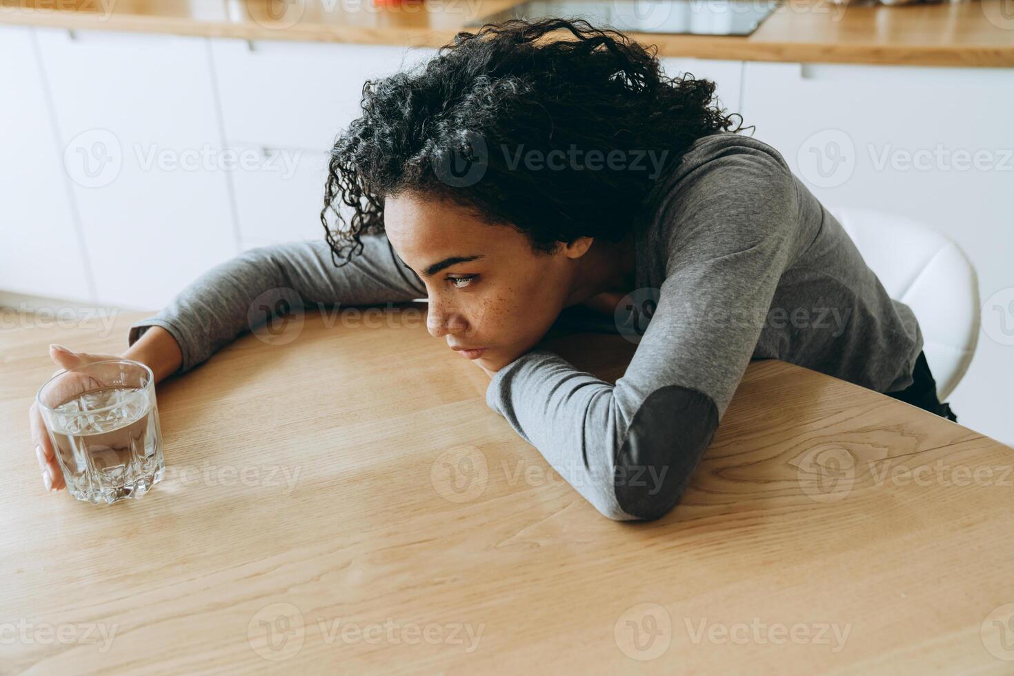 jonge zwarte vrouw die naar waterglas kijkt terwijl ze in de keuken zit foto