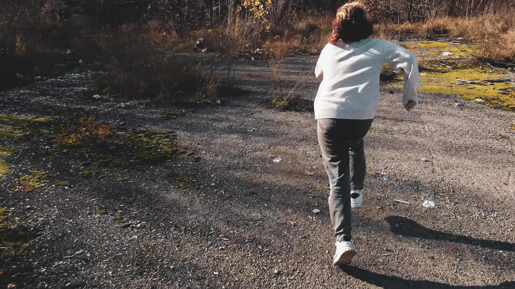 een tienermeisje loopt snel weg van een maniak op een landelijke weg in de buurt van een vuilstort foto