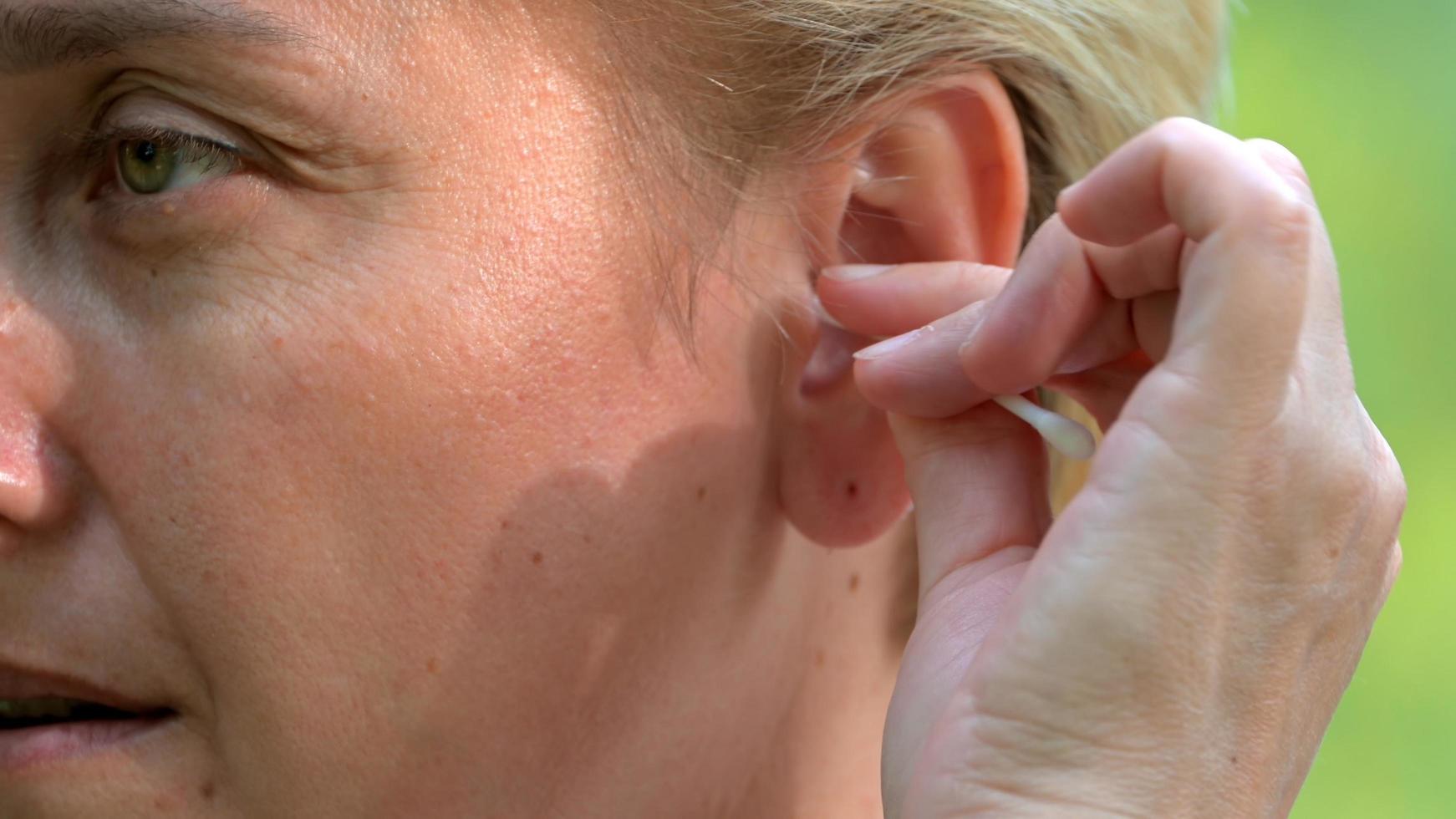 een meisje met blond haar en een kort kapsel maakt haar oor schoon met een wattenstaafje close-up foto