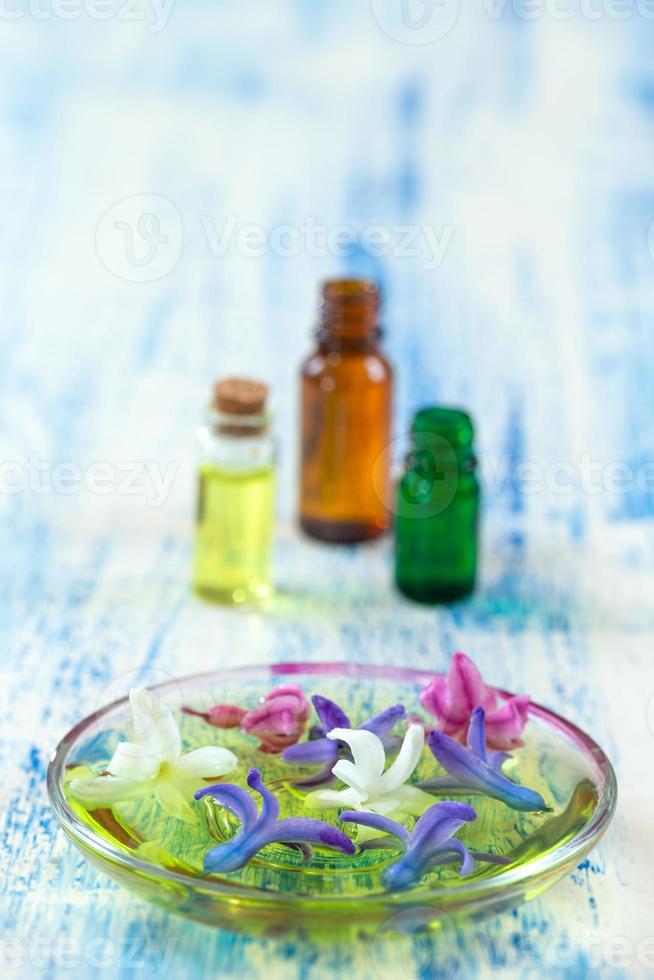 blauwe witte en roze bloemen van hyacint in een keramische kom met druppelaar voor etherische olie en fles op achtergrond foto