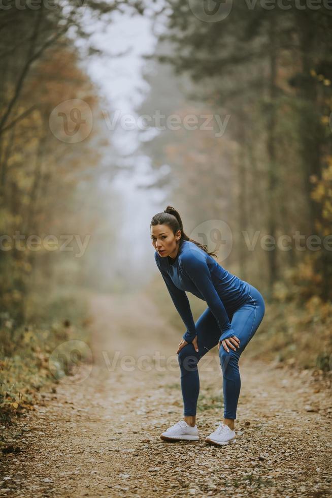 jonge vrouw neemt een pauze tijdens het sporten in de buitenlucht op het bospad in de herfst foto