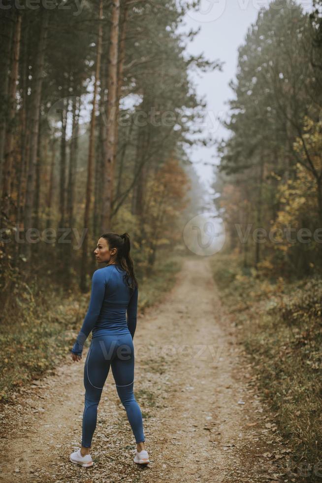 jonge vrouw neemt een pauze tijdens het sporten in de buitenlucht op het bospad in de herfst foto