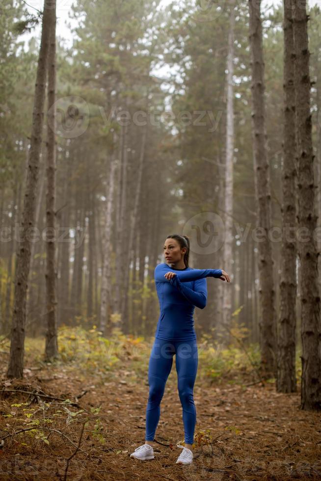 jonge vrouw in blauw trainingspak die zich uitstrekt voor de training in het herfstbos foto