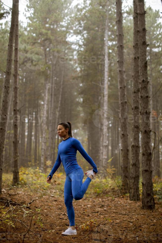 jonge vrouw in blauw trainingspak die zich uitstrekt voor de training in het herfstbos foto