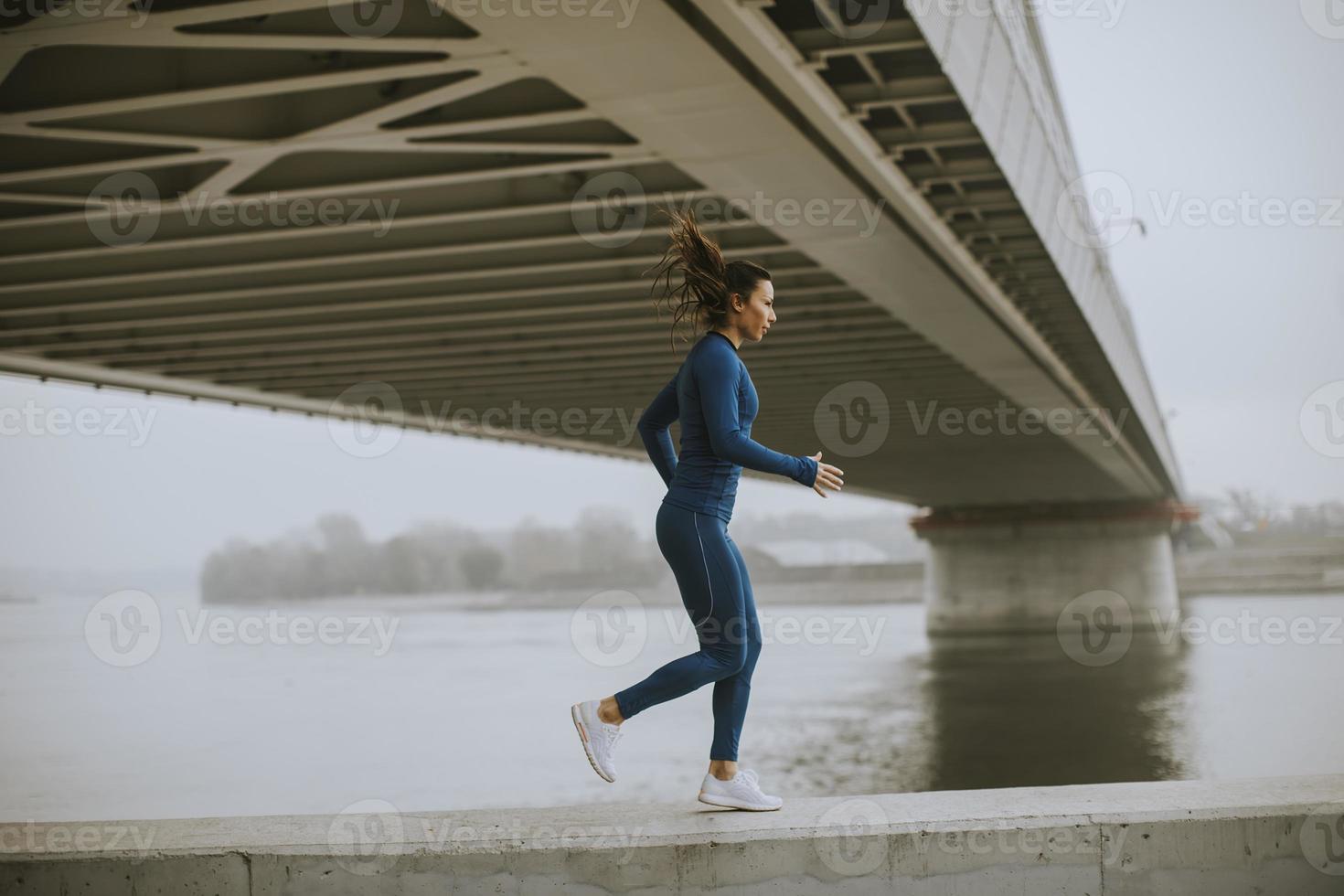 jonge vrouw in blauw trainingspak die op herfstochtend langs de rivier loopt foto