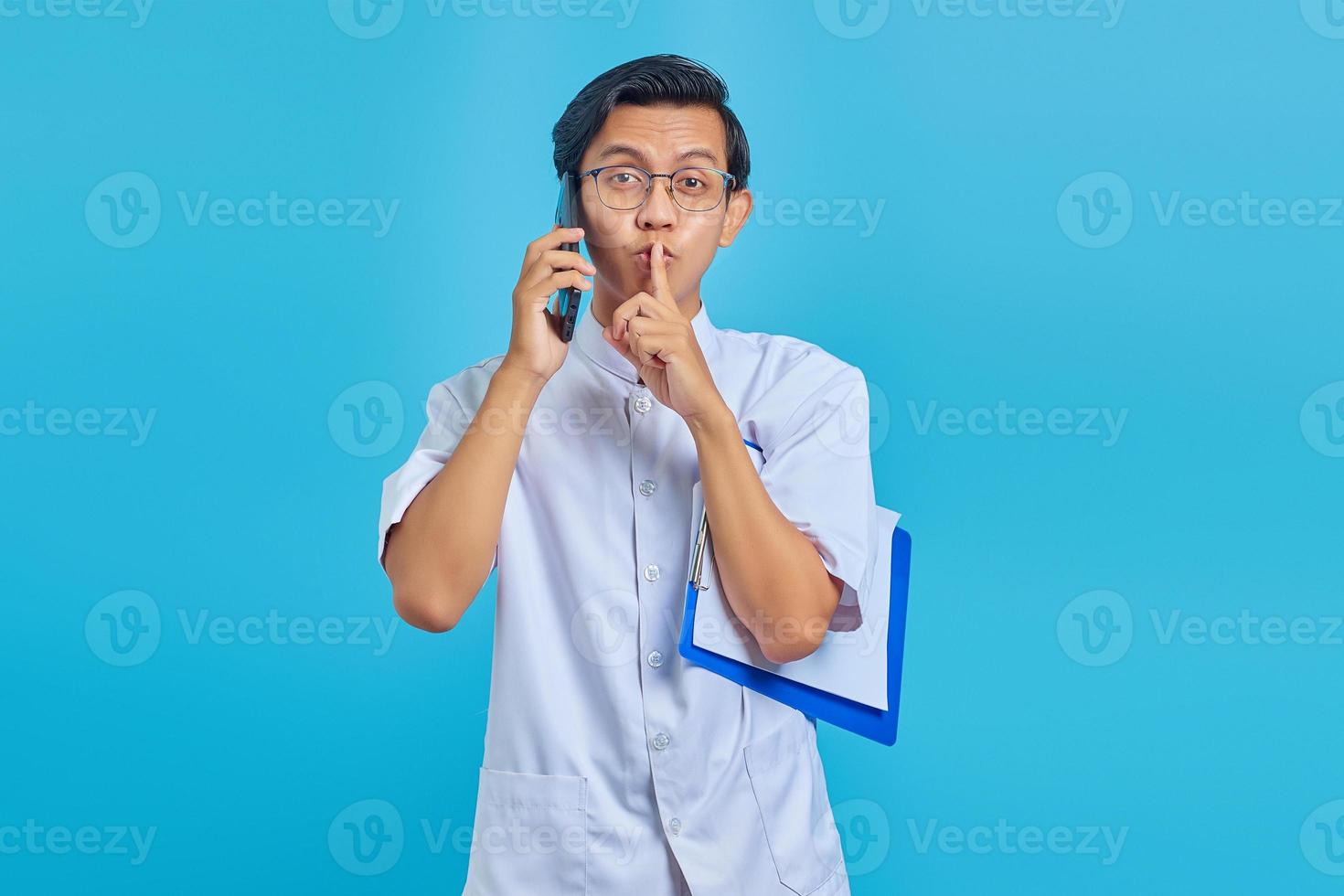 verpleger praten op mobiel klembord vasthouden en stil gebaar maken op gele achtergrond foto