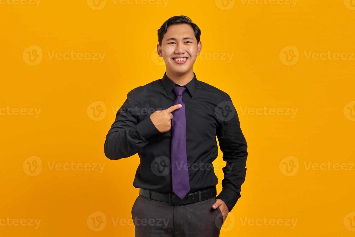 portret van lachende jonge Aziatische zakenman die met trots naar zichzelf wijst op gele achtergrond foto