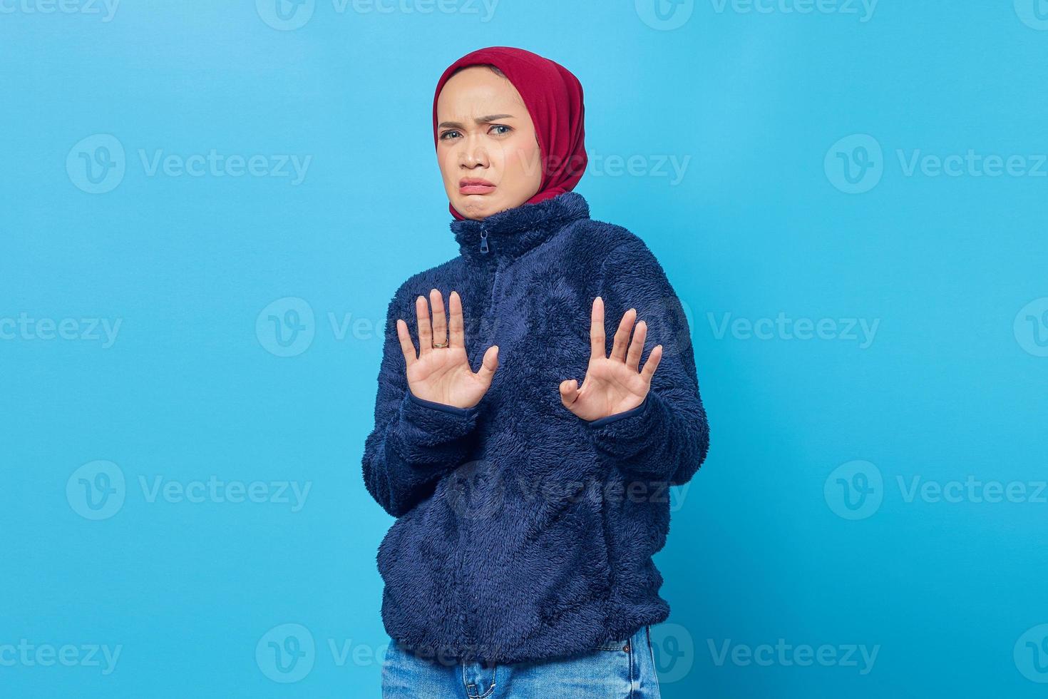 jonge aziatische vrouw die stopgebaar met handpalmen doet die over blauwe achtergrond worden geïsoleerd foto