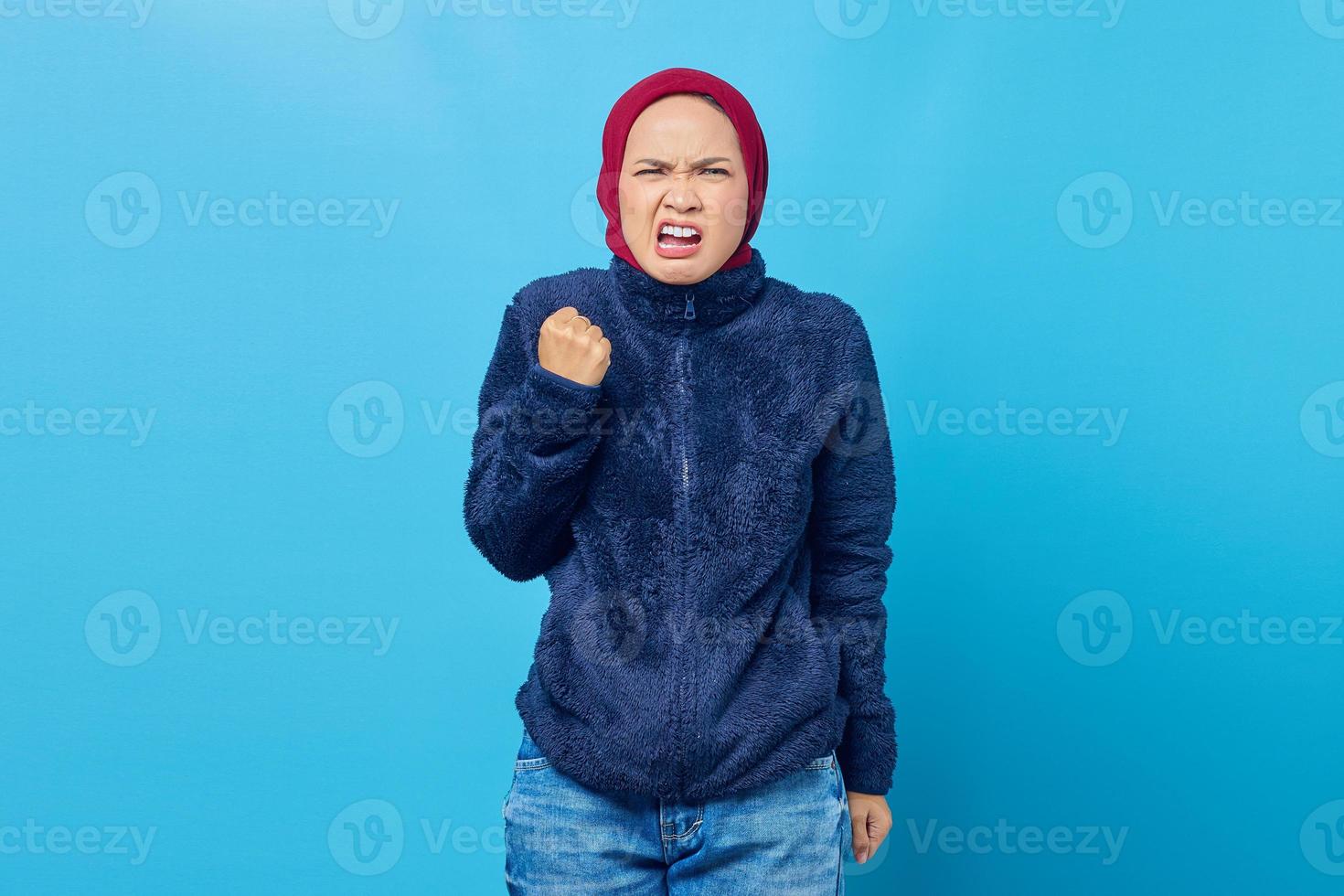 Boze jonge Aziatische vrouw schreeuwen met opgeheven hand geïsoleerd op blauwe achtergrond foto