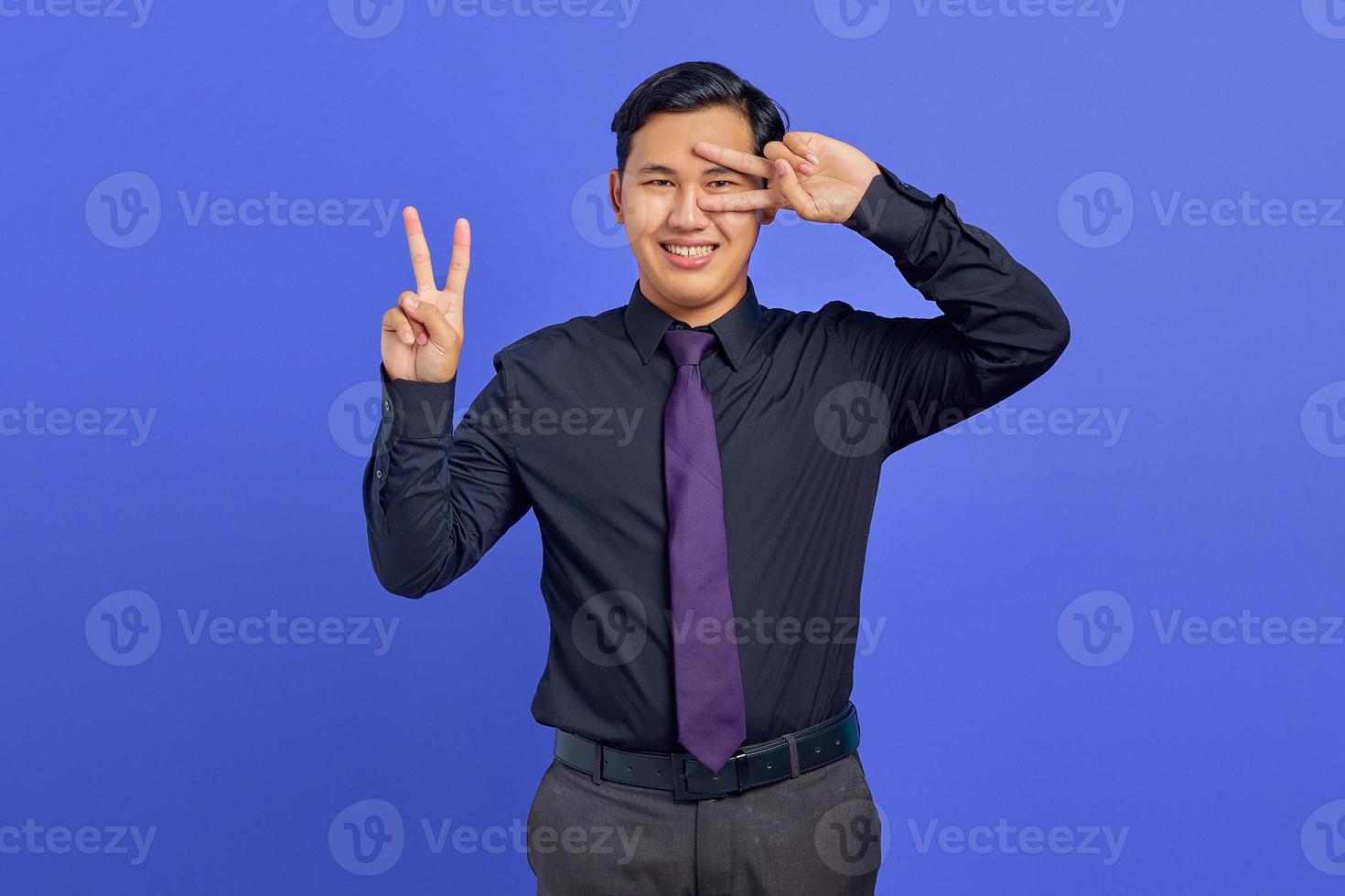 foto van een glimlachende knappe zakenman die een vredesteken boven de ogen op een paarse achtergrond toont